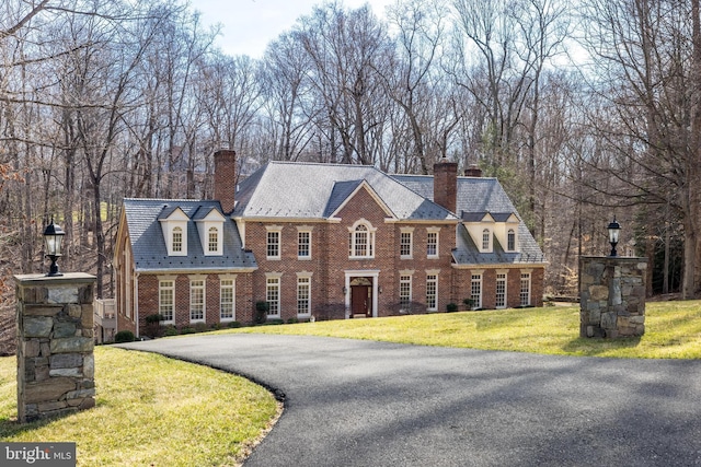 colonial home featuring a front yard, driveway, a high end roof, a chimney, and brick siding