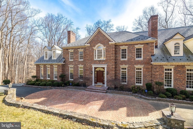 colonial-style house with a high end roof, brick siding, and a chimney