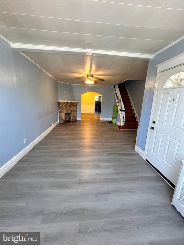 unfurnished living room featuring baseboards, arched walkways, stairway, wood finished floors, and a fireplace