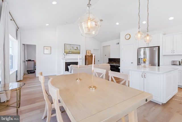 dining room with light wood finished floors, recessed lighting, a fireplace, a toaster, and lofted ceiling