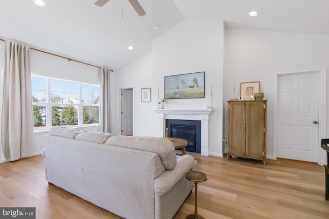 living room featuring light wood-type flooring, recessed lighting, a glass covered fireplace, high vaulted ceiling, and a ceiling fan