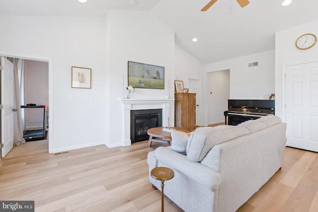 living room featuring visible vents, high vaulted ceiling, light wood-style flooring, a glass covered fireplace, and baseboards