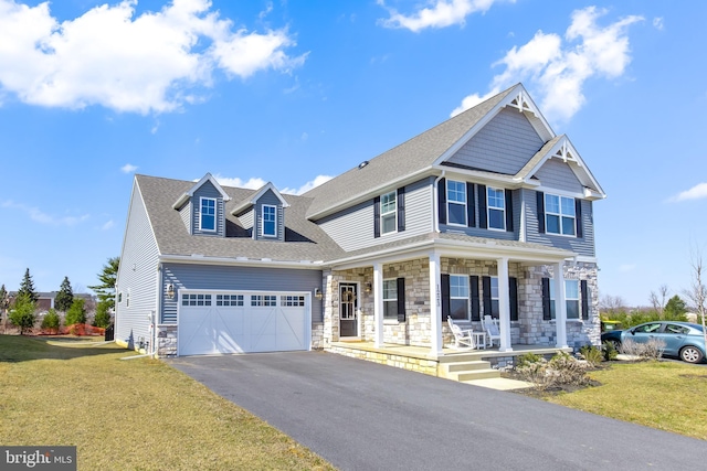 view of front of property with a front lawn, covered porch, a garage, stone siding, and driveway