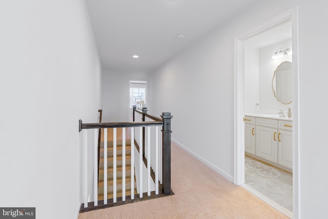 hallway with a sink, an upstairs landing, light colored carpet, and baseboards