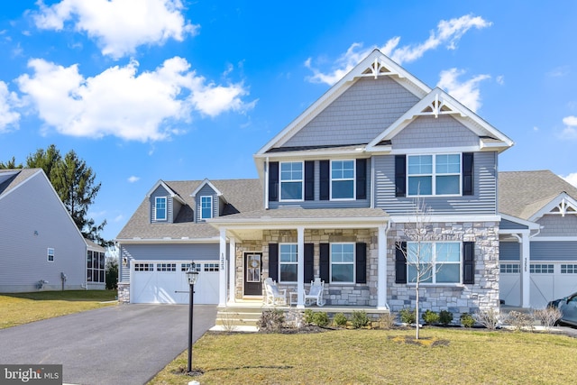 craftsman-style home featuring a porch, a front yard, driveway, stone siding, and an attached garage