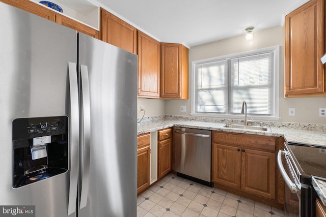 kitchen with light stone countertops, brown cabinetry, appliances with stainless steel finishes, and a sink