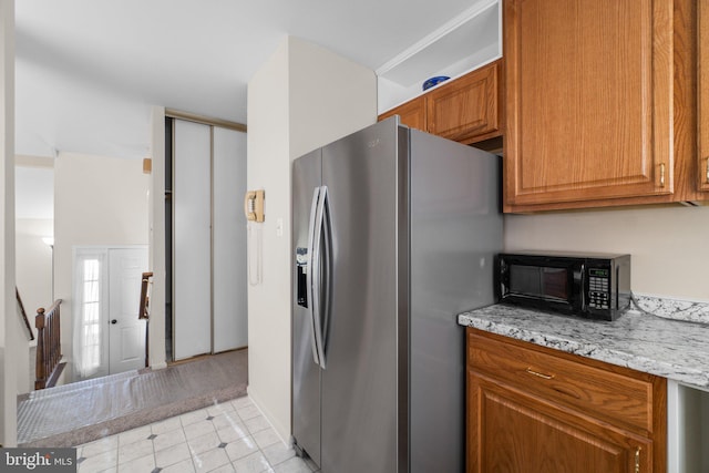 kitchen featuring brown cabinetry, light stone counters, black microwave, and stainless steel fridge with ice dispenser