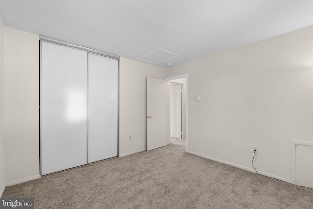 unfurnished bedroom with a closet, attic access, and carpet