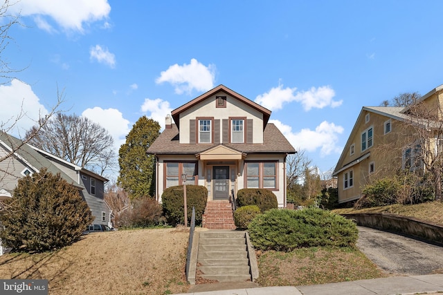 view of front facade featuring stairs, roof with shingles, and stucco siding