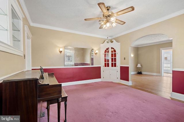 interior space featuring baseboards, carpet floors, ornamental molding, arched walkways, and a ceiling fan