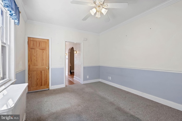 spare room featuring a ceiling fan, baseboards, arched walkways, crown molding, and carpet flooring