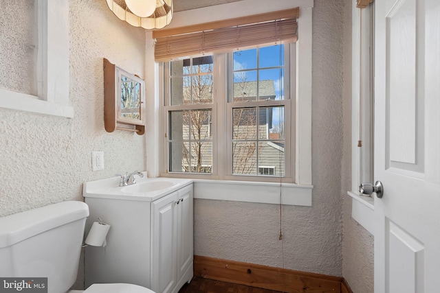 half bathroom with toilet, vanity, plenty of natural light, and a textured wall