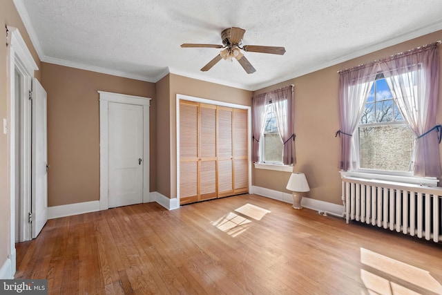 unfurnished bedroom with crown molding, light wood-style flooring, radiator heating unit, and a closet