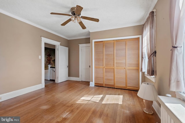 unfurnished bedroom with a ceiling fan, baseboards, light wood-style floors, a textured ceiling, and crown molding