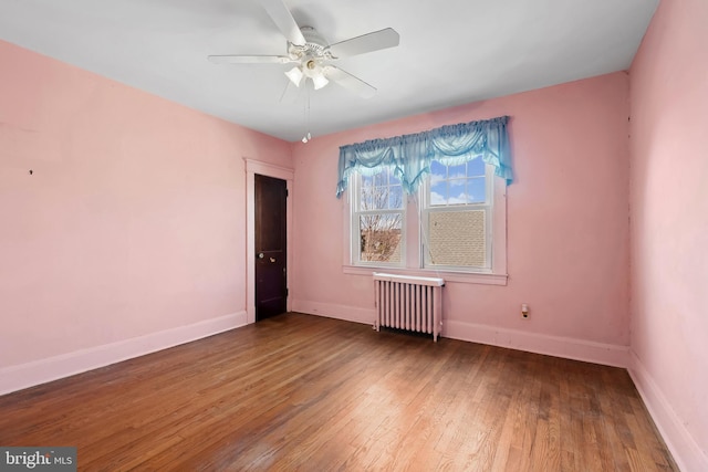 spare room featuring ceiling fan, baseboards, wood finished floors, and radiator heating unit