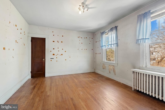 unfurnished room with baseboards, radiator, and hardwood / wood-style flooring