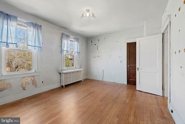 empty room featuring light wood-type flooring, baseboards, and radiator