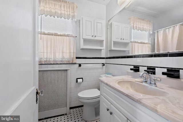 bathroom with toilet, curtained shower, tile walls, wainscoting, and vanity