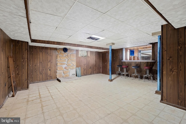 basement featuring tile patterned floors, a dry bar, and wood walls