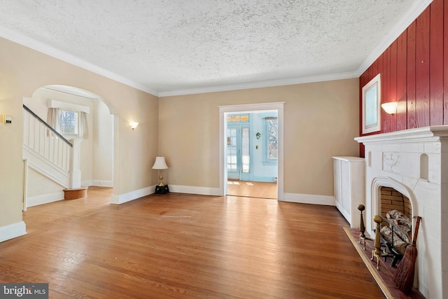 unfurnished living room featuring arched walkways, light wood-style floors, a fireplace, and stairs