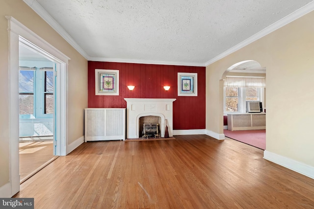 unfurnished living room featuring arched walkways, crown molding, radiator heating unit, and wood finished floors