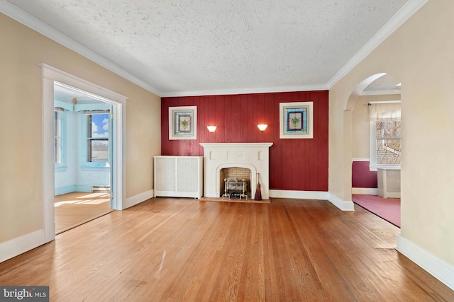 unfurnished living room featuring arched walkways, wood finished floors, radiator heating unit, and ornamental molding