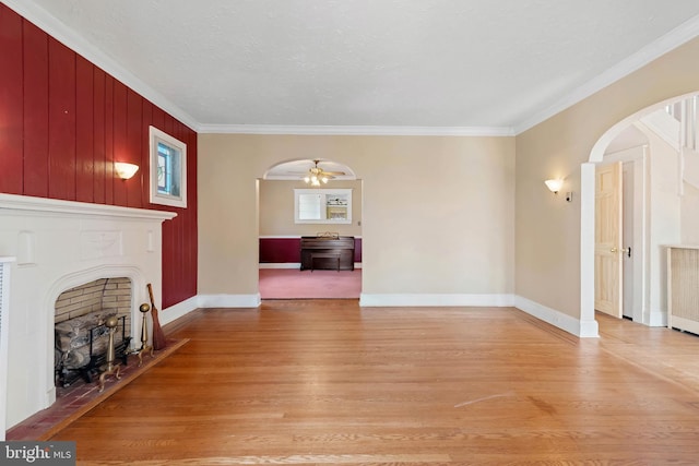 unfurnished living room with arched walkways, a fireplace, light wood-type flooring, and ornamental molding