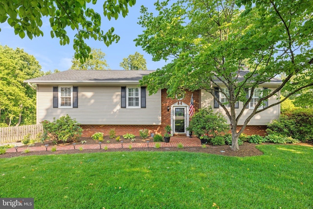 split foyer home with a front yard, brick siding, and fence