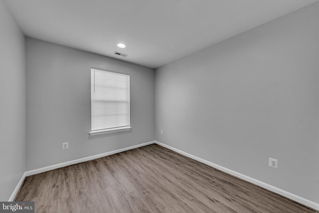 spare room with wood finished floors, visible vents, and baseboards