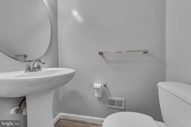 bathroom with toilet, a sink, wood finished floors, visible vents, and baseboards