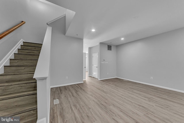 unfurnished living room with stairway, wood finished floors, visible vents, and baseboards