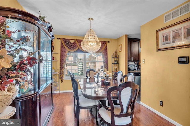 dining area featuring visible vents, a notable chandelier, baseboards, and wood finished floors