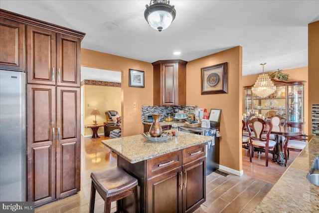 kitchen with light stone counters, light wood-style flooring, built in refrigerator, a kitchen breakfast bar, and backsplash