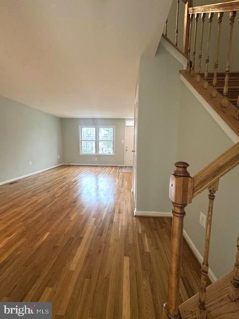 unfurnished living room with stairs, baseboards, and wood finished floors