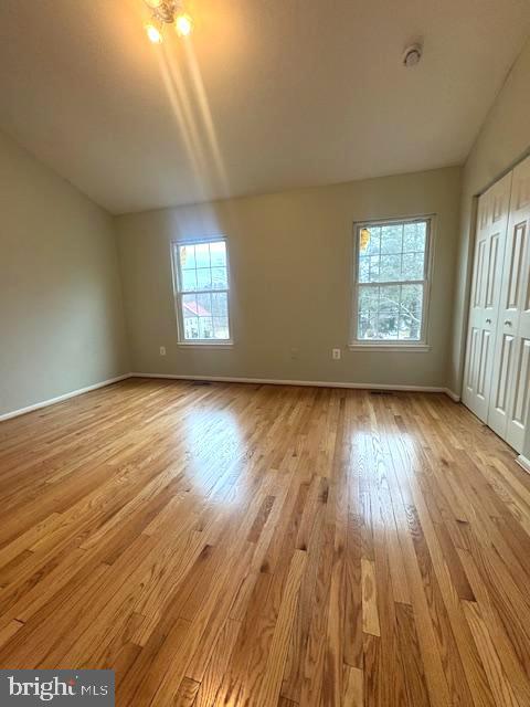 unfurnished bedroom featuring lofted ceiling, a closet, wood finished floors, and baseboards