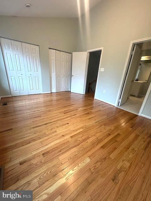 unfurnished bedroom featuring high vaulted ceiling, two closets, and wood finished floors