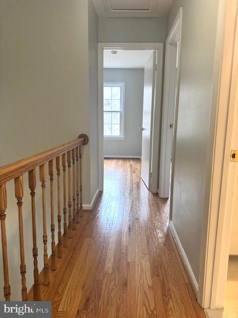 hall with an upstairs landing, attic access, baseboards, and light wood finished floors