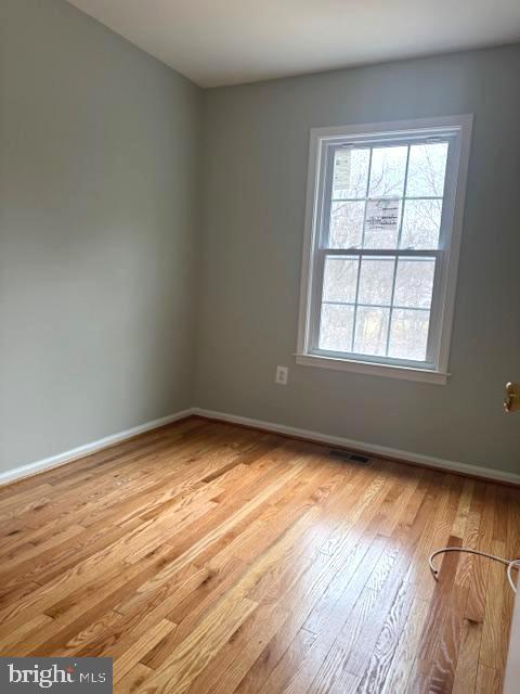 empty room with light wood-type flooring, visible vents, and baseboards