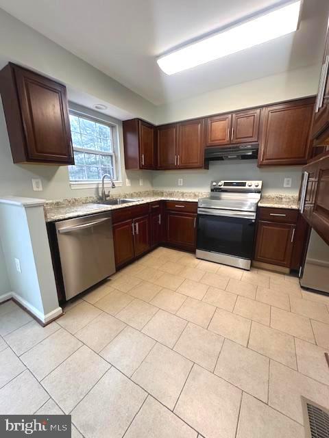 kitchen with stainless steel appliances, light countertops, a sink, dark brown cabinets, and under cabinet range hood