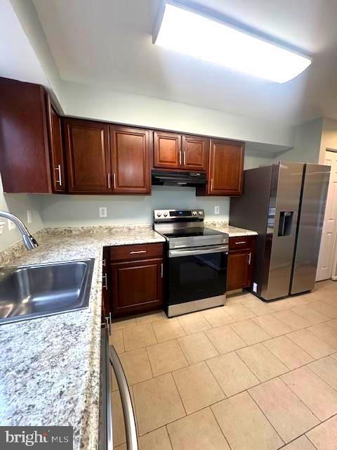 kitchen featuring stainless steel appliances, light stone counters, a sink, and under cabinet range hood