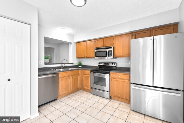 kitchen with a sink, stainless steel appliances, dark countertops, and light tile patterned floors