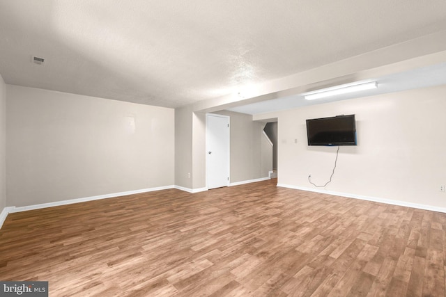 finished basement featuring visible vents, a textured ceiling, baseboards, and wood finished floors