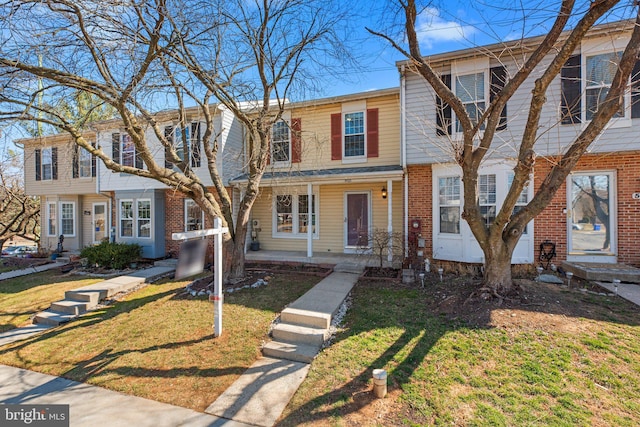 view of property with a front lawn, brick siding, and covered porch