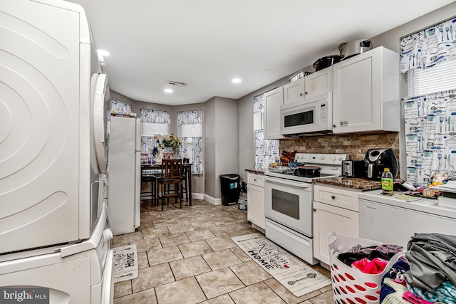 kitchen featuring stacked washer and clothes dryer, visible vents, backsplash, white cabinetry, and white appliances