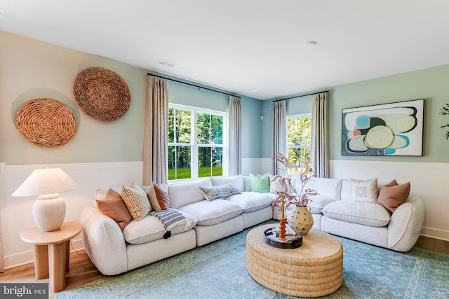 living room with a wainscoted wall, visible vents, and wood finished floors