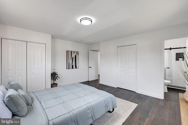 bedroom featuring dark wood-style floors, a barn door, ensuite bathroom, and baseboards