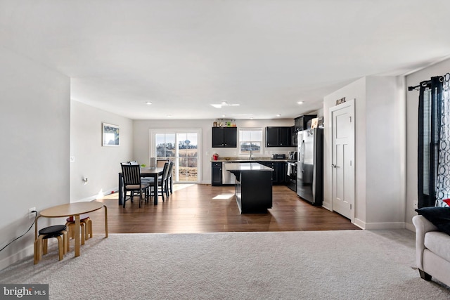 kitchen with dark cabinets, a kitchen island, open floor plan, freestanding refrigerator, and dark carpet