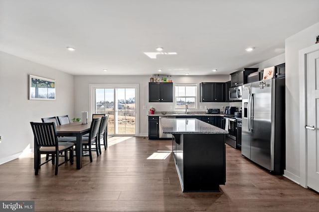 kitchen featuring light stone counters, dark wood-style flooring, a sink, a kitchen island, and appliances with stainless steel finishes