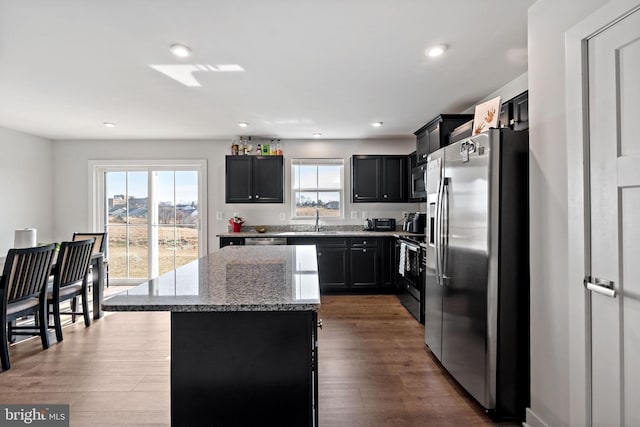 kitchen featuring appliances with stainless steel finishes, light stone counters, a center island, dark cabinetry, and a sink