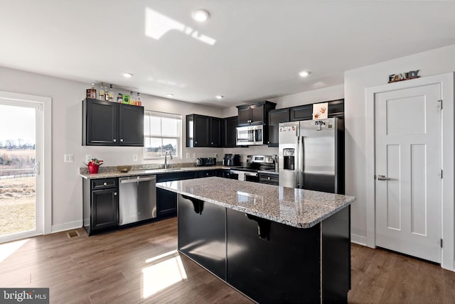 kitchen featuring dark wood-style flooring, stainless steel appliances, recessed lighting, a kitchen island, and light stone countertops